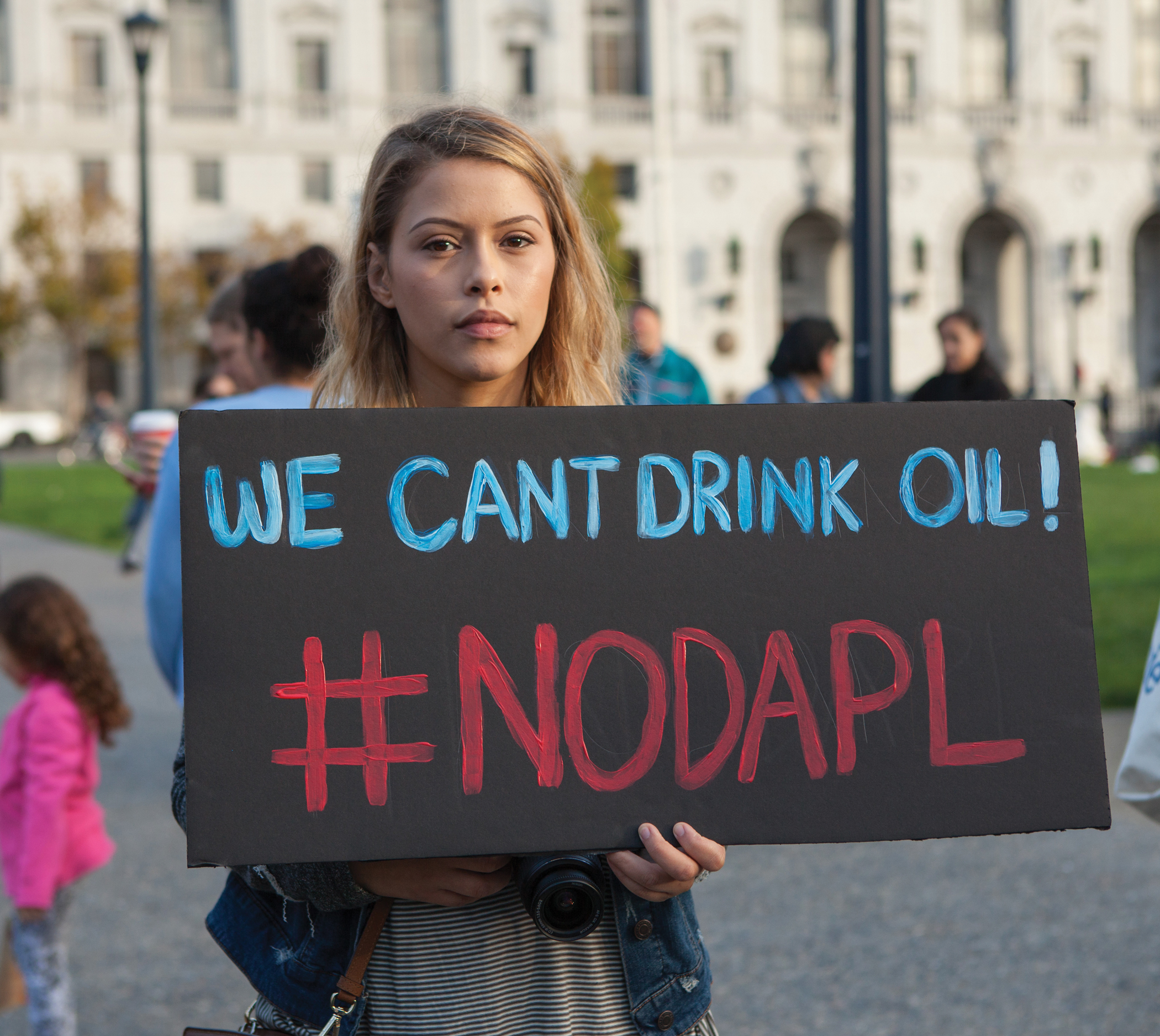 Female Protestor holding a sign that states "We Cant Drink Oil #NoDAPL