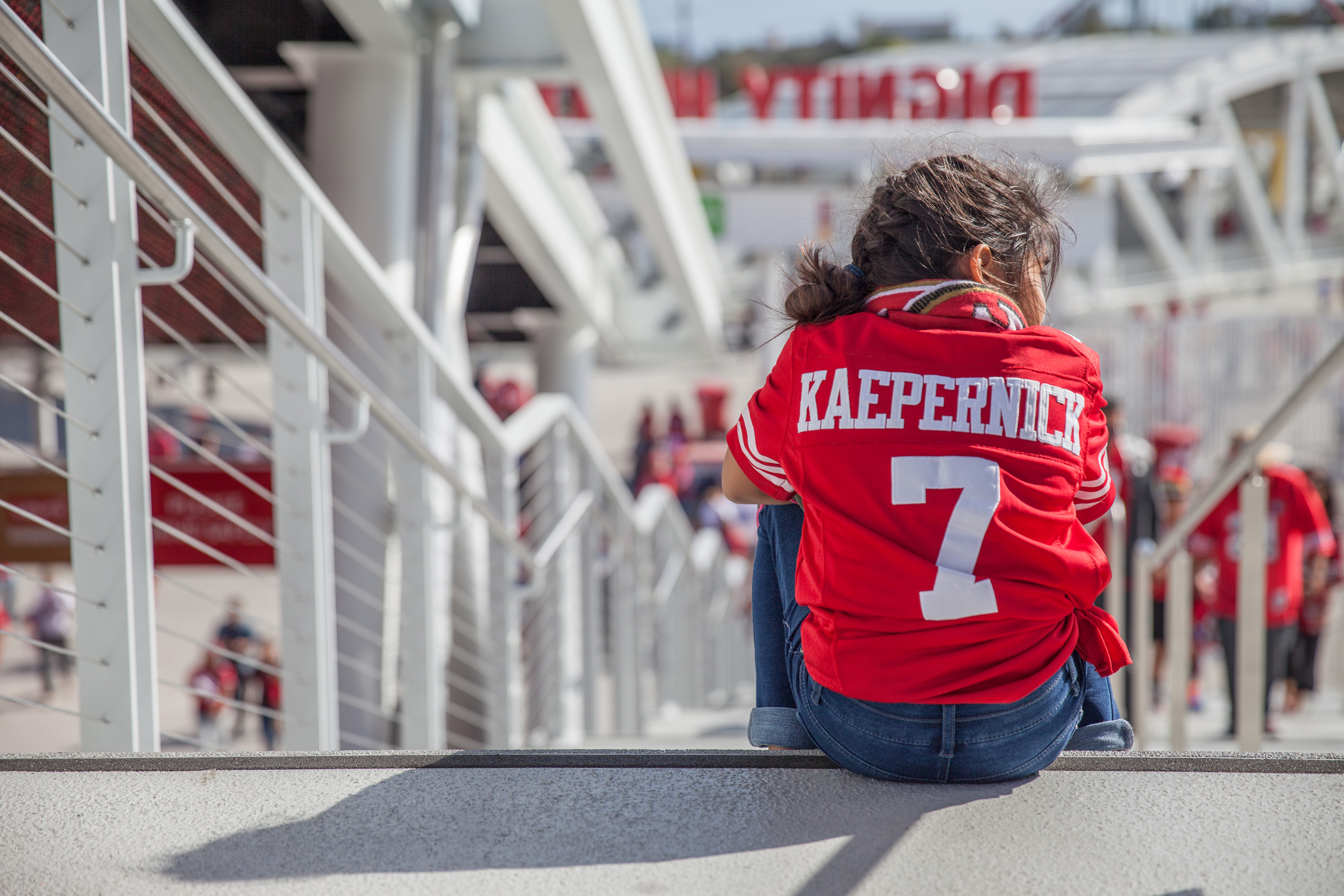 Young girl wearing a Kaepernick jersey sitting in the stands waiting