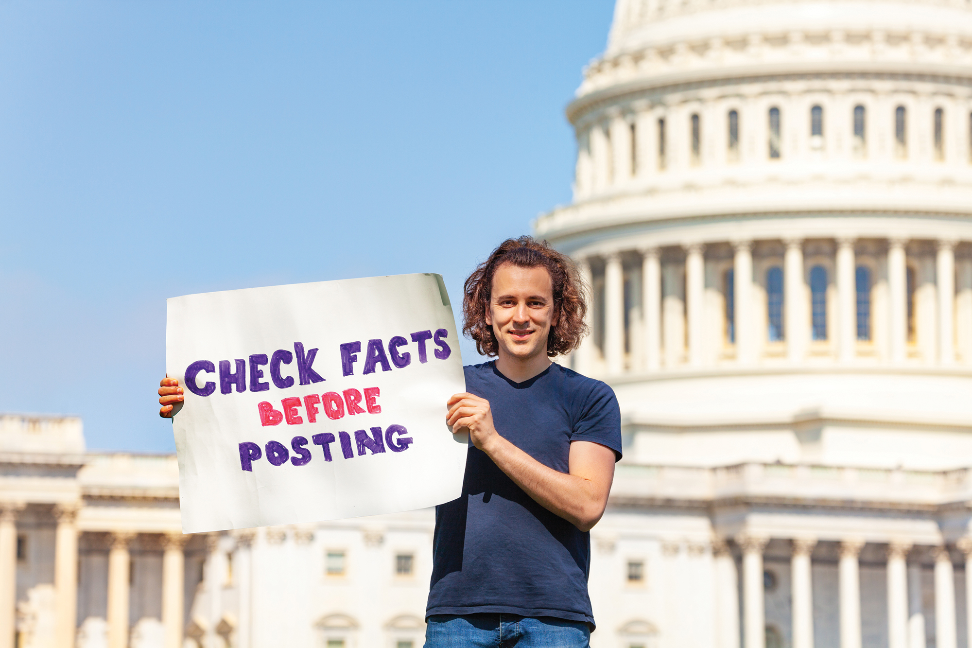 Protestor standing in front of U.S. Capitol holding sign that reads "Check Facts Before Posting"