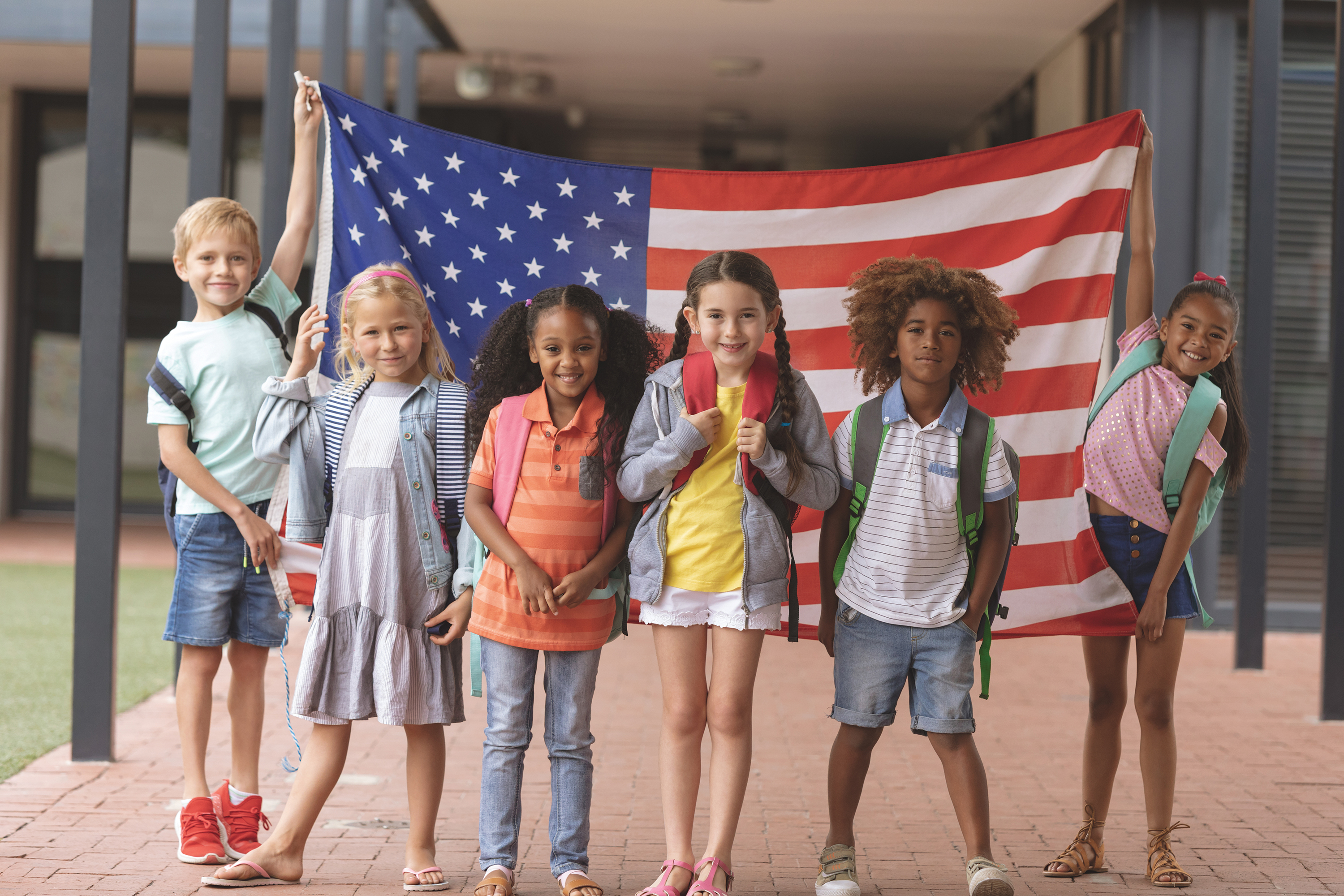 Front view of happy students standing in front of and holding American flag