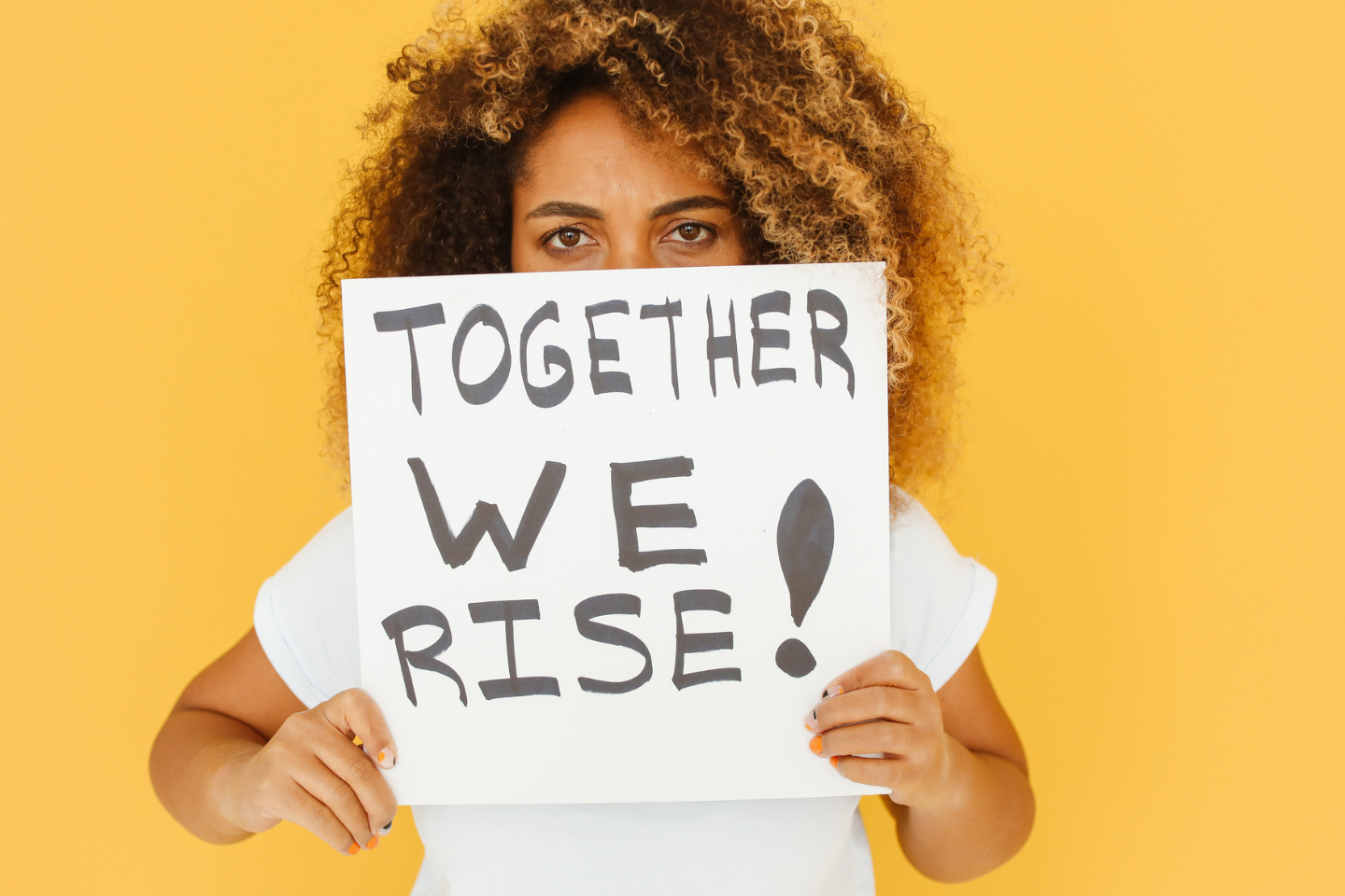 Female holding a sing in front of her face that reads "Together We Rise"