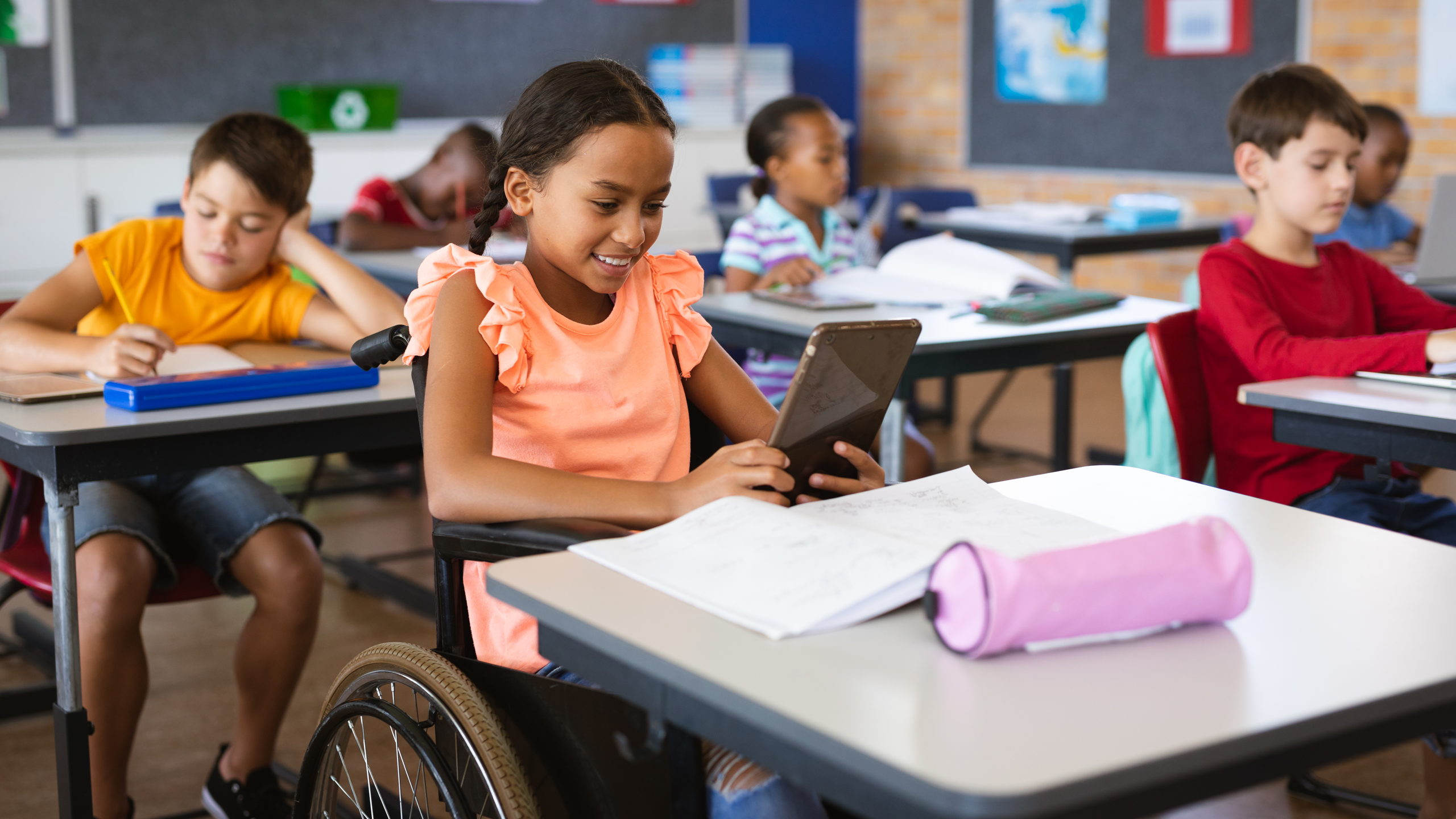 Disabled African American girl using a tablet while sitting in wheelchair at elementary school