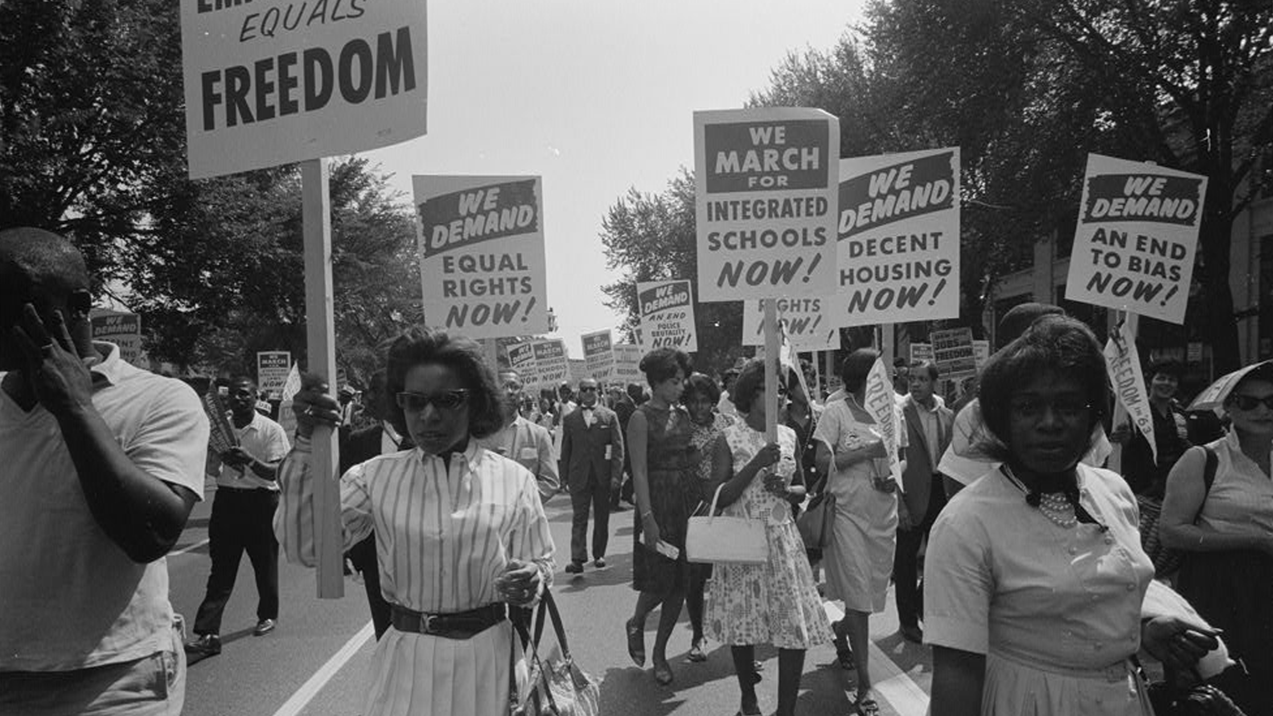 A procession of African Americans carrying signs for equal rights, integrated schools, decent housing