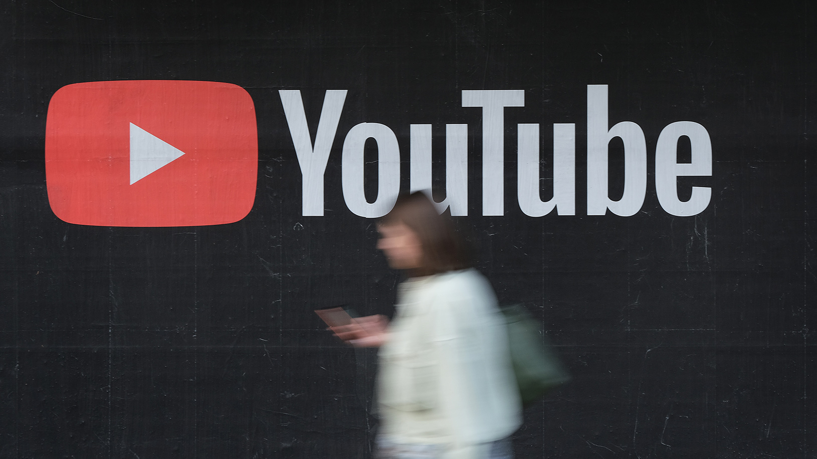 blurred person with a smartphone walking in front of the YouTube logo