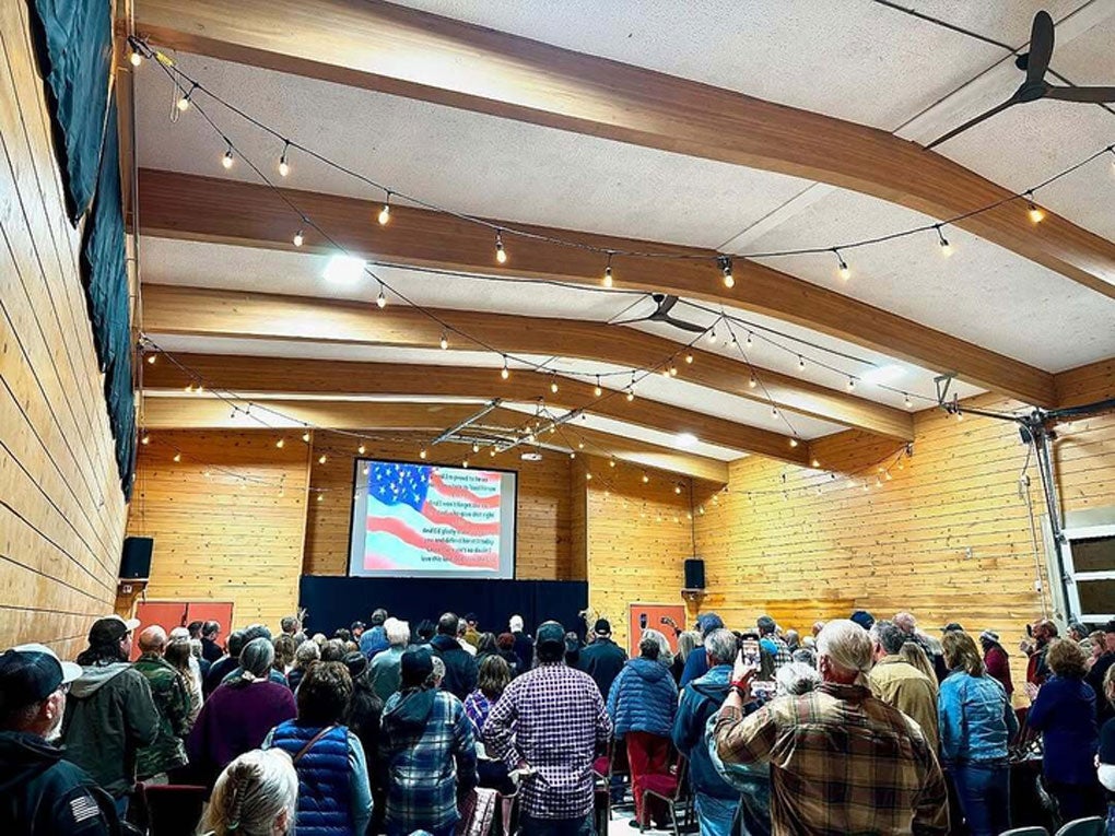 A large group of people standing in a meeting hall watching a presentation on a projection screen.