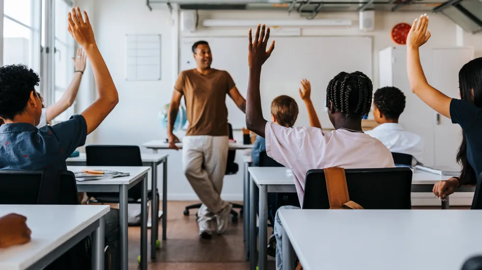Rear view of students in class with their hands raised