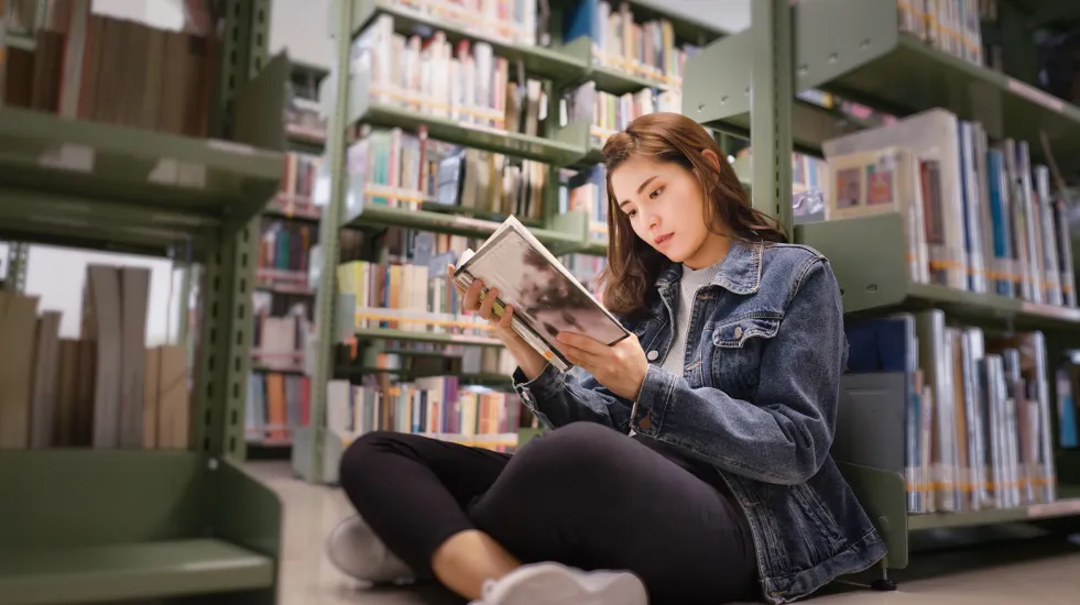 Student sitting on the floor in a library reading