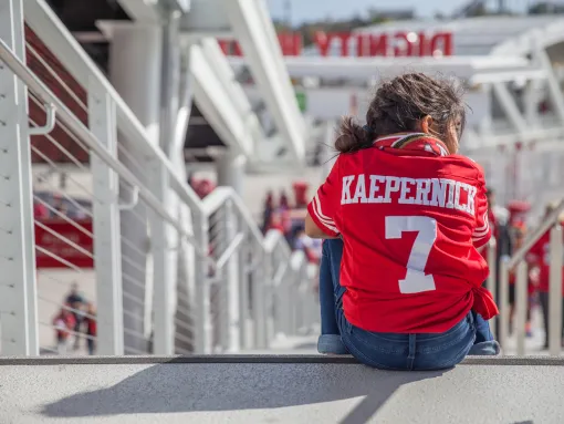 Young girl wearing a Kaepernick jersey sitting in the stands waiting