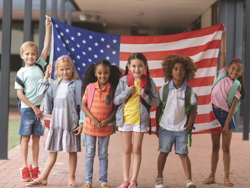 Front view of happy students standing in front of and holding American flag