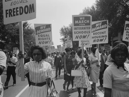 A procession of African Americans carrying signs for equal rights, integrated schools, decent housing