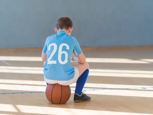 Rear view of boy wearing a jersey and other sports attire and sitting on a ball