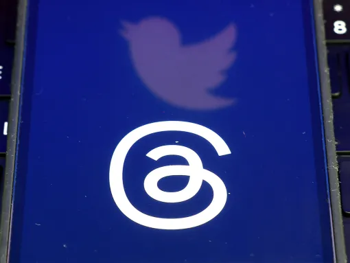 Phone screen showing both the Threads and Twitter logos on top of a computer keyboard
