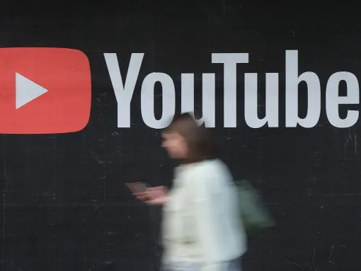 blurred person with a smartphone walking in front of the YouTube logo