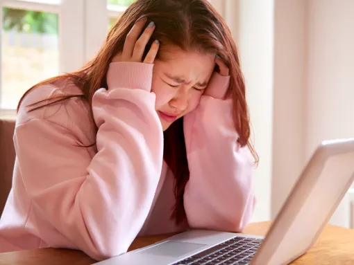 Distraught girl with eyes closed sitting in front of laptop