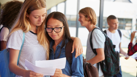 Two girls sharing exam results in school corridor