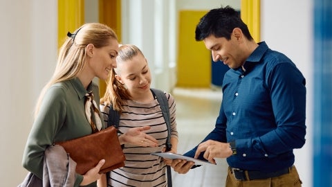 Parent and child talking to a teacher in a hallway of a school
