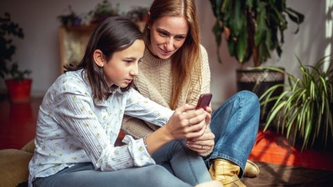 Tween looking at phone with a supportive parent in a living room