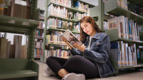 Student sitting on the floor in a library reading